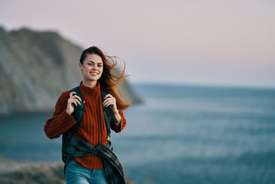 Smiling young woman standing against sea against sky