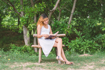 Full length of young woman sitting on chair against trees