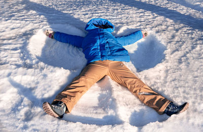 Young woman in a blue jacket making a snow angel in the snow winter joy and fun