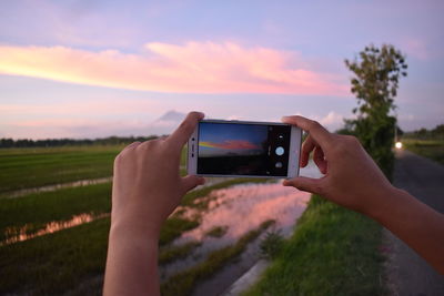 Midsection of person photographing mobile phone against sky