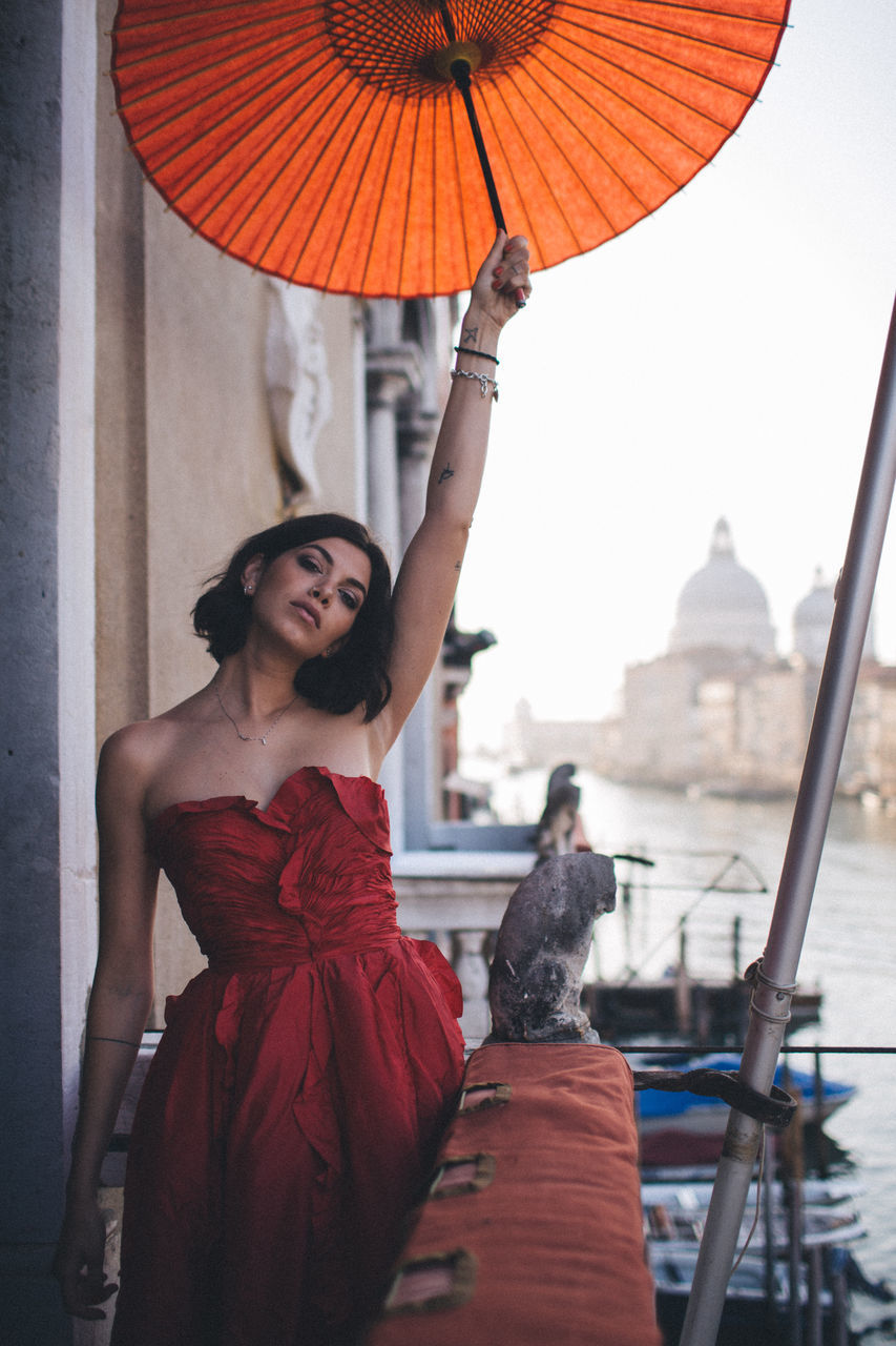 architecture, real people, adult, women, umbrella, people, red, built structure, building exterior, two people, dress, orange color, young adult, young women, water, focus on foreground, clothing, three quarter length, casual clothing