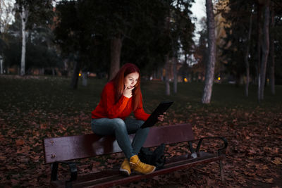 Young woman using phone while sitting on sidewalk