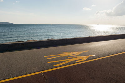 Yellow markings on promenade by sea against sky