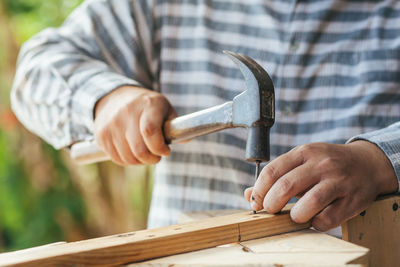 Midsection of man hammering nail in wood at workshop