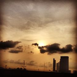 Silhouette of buildings against cloudy sky at sunset