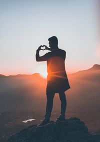 Silhouette man photographing on rock against sky during sunset