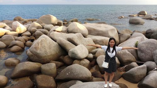 Portrait of young woman standing with arms outstretched on rocks at beach