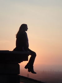 Side view full length of silhouette woman sitting against sky during sunset