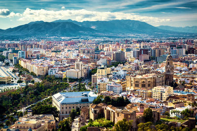 Cityscape by mountains against cloudy sky