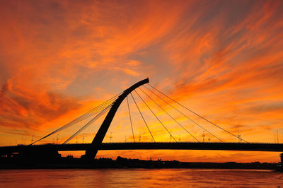 Silhouette bridge over sea against sky during sunset