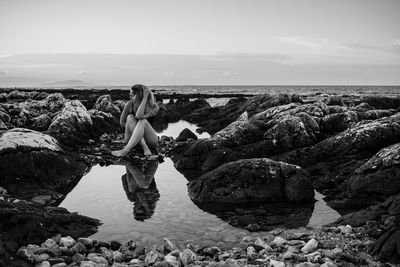 Woman sitting on rock by sea against sky