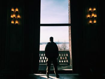 Rear view of silhouette man standing against window