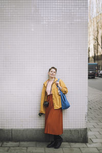 Portrait of mid adult woman with bag and camera standing on footpath