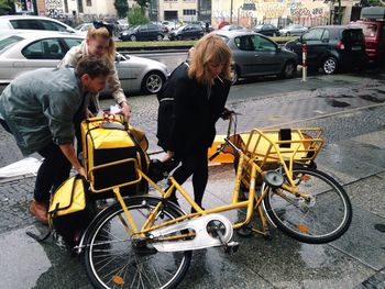 Man and woman helping mid adult lifting bicycle on sidewalk