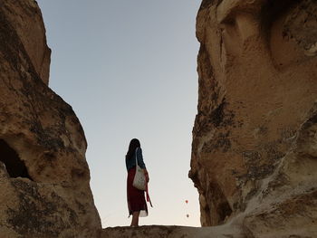 Rear view of woman standing on rock against sky