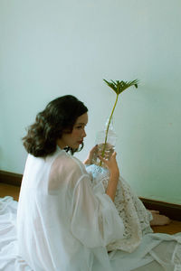Side view of woman holding flowering plant sitting at home