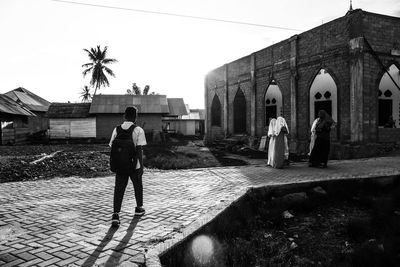 Rear view of people standing by palm trees and buildings