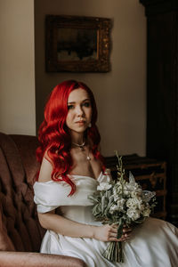 Red haired bride sitting in the armchair with bouquet