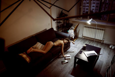 Woman reading book while lying down on sofa at home