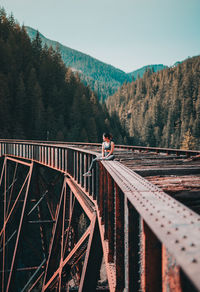 Woman sitting on damaged bridge against sky