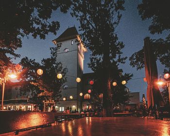 Illuminated street amidst buildings against sky at night