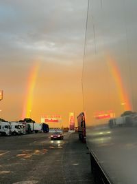 Cars on road against rainbow in sky during sunset