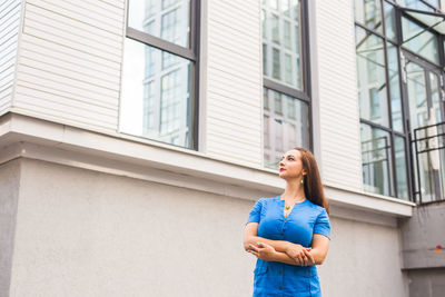 Young woman looking away while standing against building