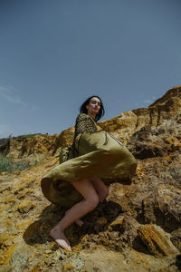 Man sitting on rock against sky