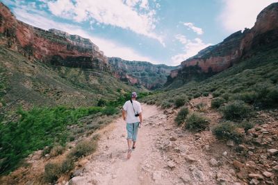 Rear view of man walking on rocky mountain against sky