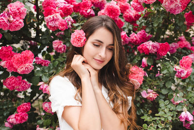 Smiling beautiful woman with long blonde hair and rose flower over bloom nature background outdoor