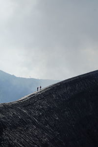 Two people climbing mountain against sky