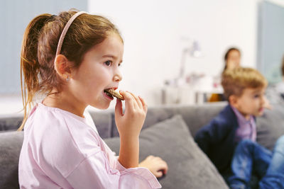 Side view of girl eating cookie while sitting on sofa