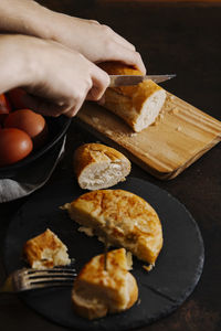 Spanish potato omelette sliced and served with bread. a woman is cutting some bread slices in the background.