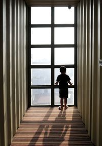 Rear view of boy looking through window in building