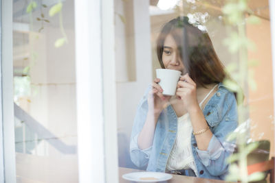 Young woman drinking coffee at window