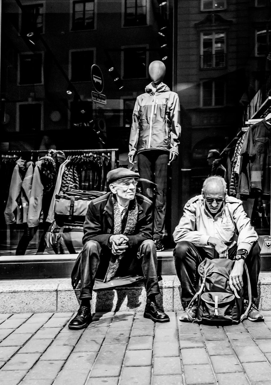 men, real people, sitting, full length, casual clothing, city, building exterior, people, day, seat, footpath, architecture, built structure, group of people, outdoors, street, lifestyles, chair, sidewalk, rear view