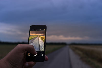 Cropped image of hands photographing country road