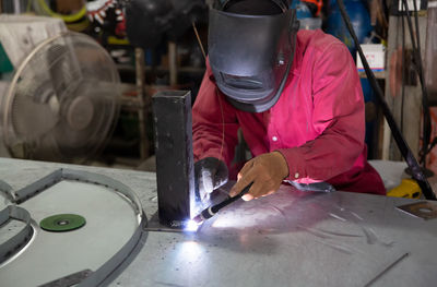 The worker is welding a steel frame in the workshop.