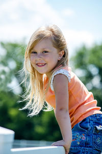 Portrait of a smiling little blond girl as she climbs on a fence