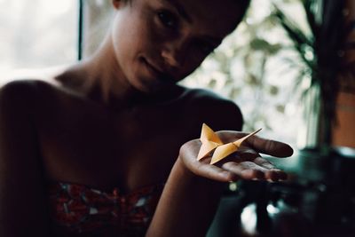 Close-up portrait of woman holding figurine butterfly at home