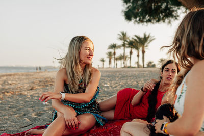 Female friends talking at beach against sky during sunset