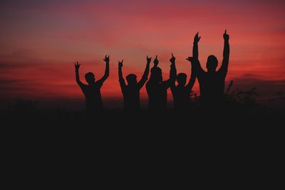 Silhouette people standing with arms raised against sky during sunset