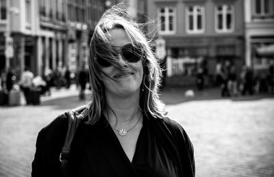 Portrait of smiling woman in sunglasses standing against buildings