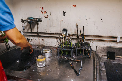 Teacher washing hands in sink near dirty paintbrushes