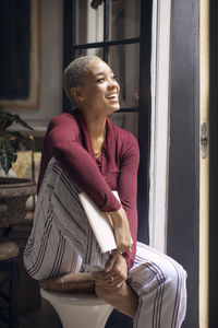 Happy woman looking away while sitting on stool at home