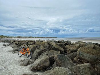 Bicycle on rock by sea against sky