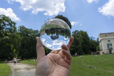 Cropped hand holding crystal ball against sky