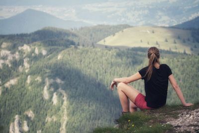 Young woman sitting on land against mountains