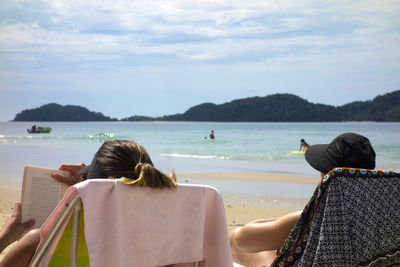 Rear view of couple sitting on beach against sky