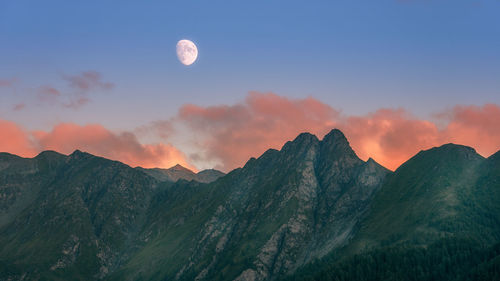 Scenic view of alps mountains and moon against sky during sunset